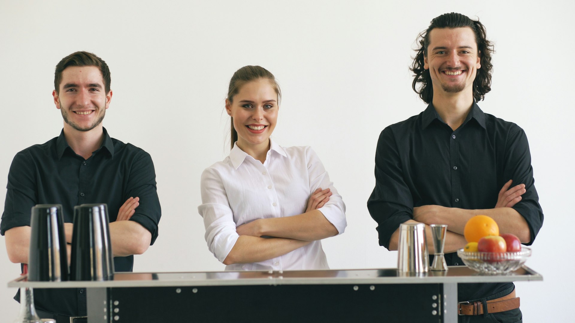 Three smiling bartenders standing behind a bar.